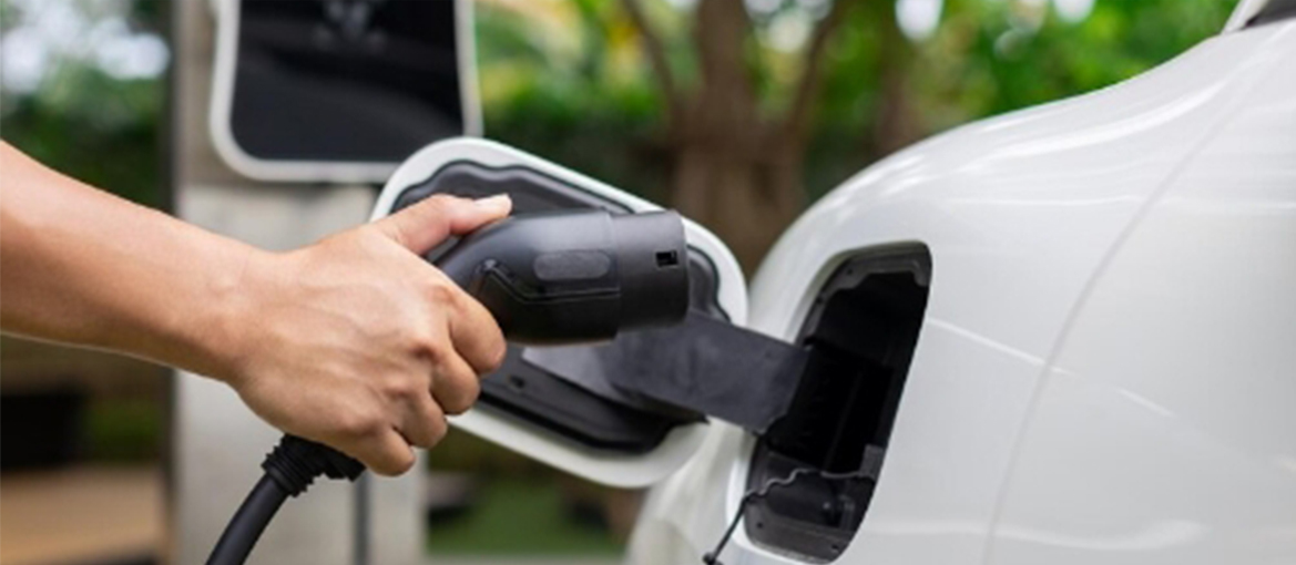 A person holds an electric car charger, demonstrating the connection between the charger and the vehicle